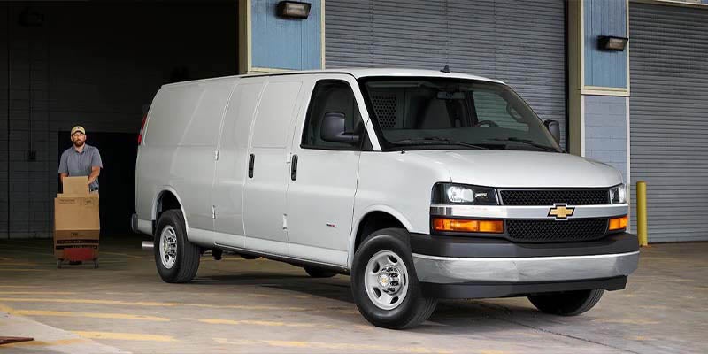 White Chevrolet Expres Van dropping off packages and worker carrying over the boxes to the warehouse